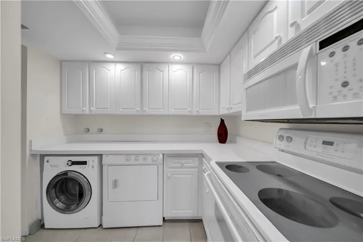 Laundry area with washing machine and dryer, a tray ceiling, light tile patterned flooring, and crown molding