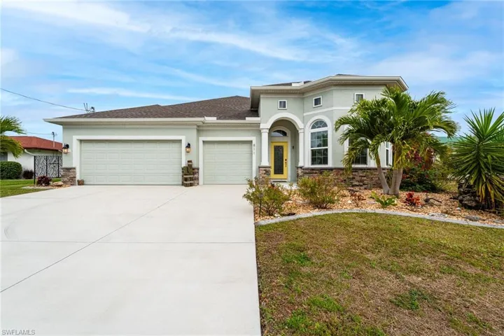 Front of Home with Beautiful Arched Windows, Tropical Landscaping & a 3-Car Garage
