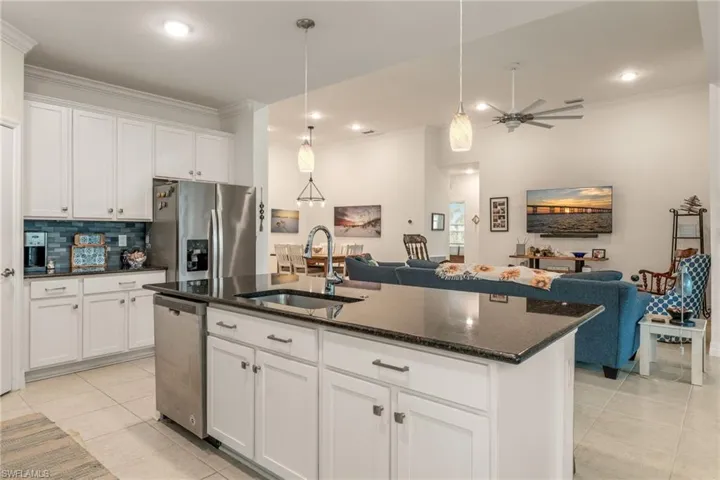 Kitchen featuring white cabinets, dark stone countertops, stainless steel appliances, open floor plan, and crown molding