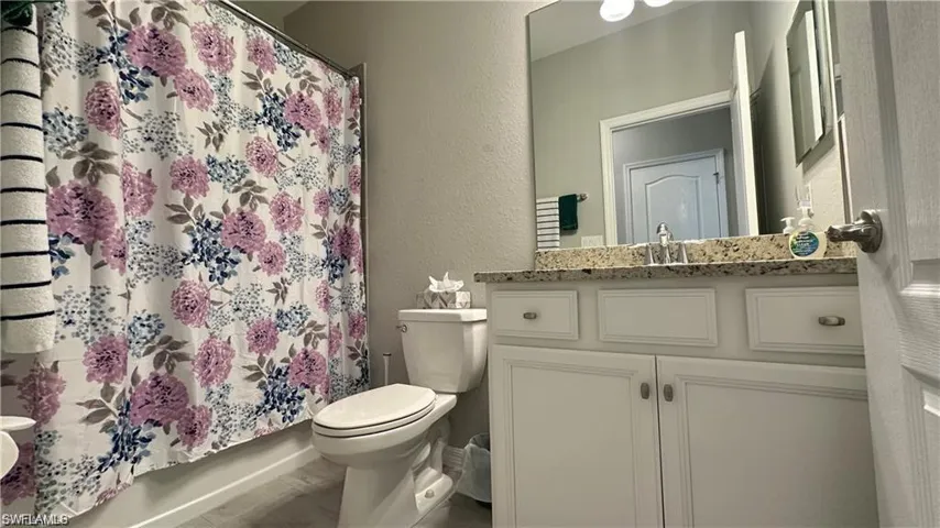 Bathroom featuring toilet, a textured wall, curtained shower, and vanity
