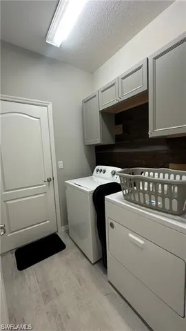 Laundry area featuring a textured ceiling, washing machine and dryer, and cabinet space