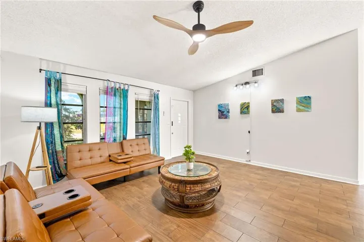 Living area featuring a ceiling fan, wood finished floors, a textured ceiling, baseboards, and visible vents