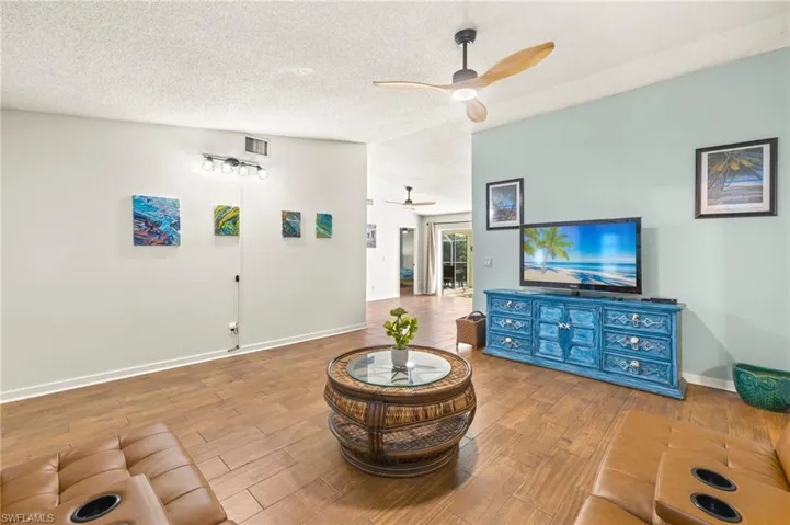 Living room featuring wood finished floors, visible vents, baseboards, a textured ceiling, and ceiling fan
