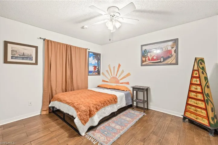 Bedroom with baseboards, a ceiling fan, wood finished floors, and a textured ceiling