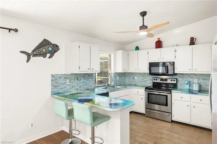 Kitchen with a sink, stainless steel electric range, black microwave, light wood-style floors, and white cabinetry