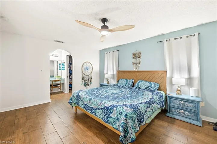 Bedroom featuring arched walkways, a textured ceiling, visible vents, a ceiling fan, and wood finished floors