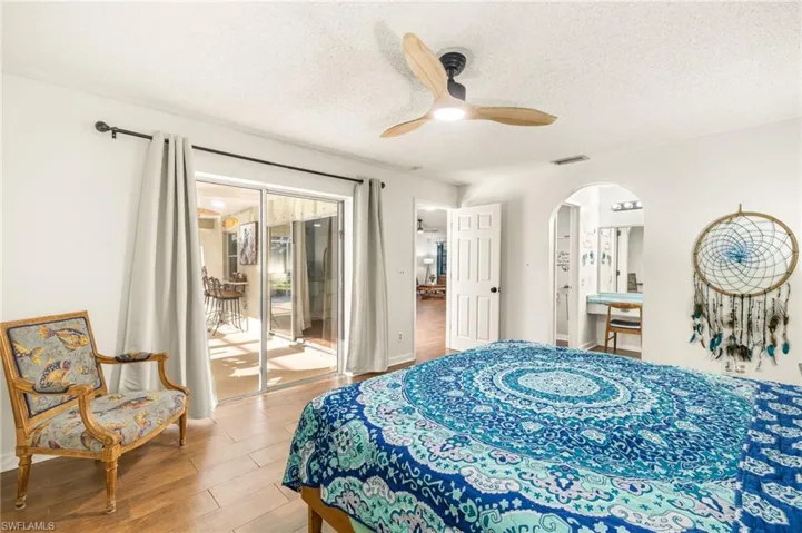 Bedroom with wood finished floors, a textured ceiling, arched walkways, access to outside, and visible vents