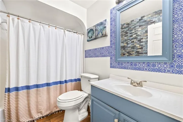 Bathroom featuring toilet, tile walls, wood finished floors, a shower with shower curtain, and vanity
