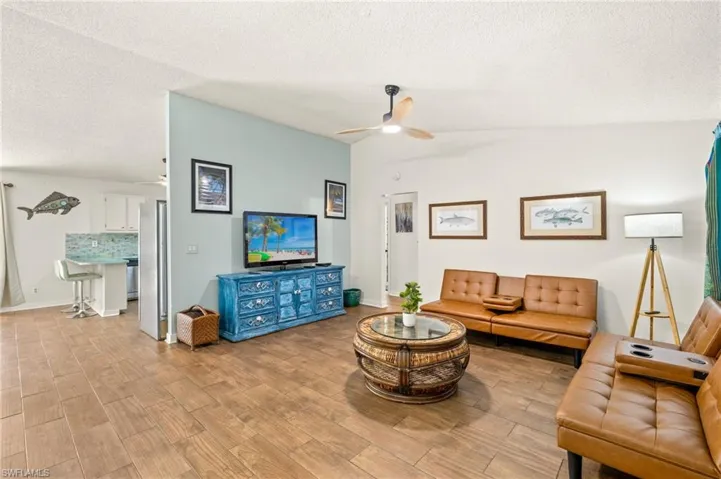 Living room with lofted ceiling, light wood-style flooring, a textured ceiling, and ceiling fan