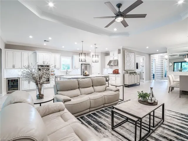Living room with sink, ceiling fan, crown molding, and beverage cooler