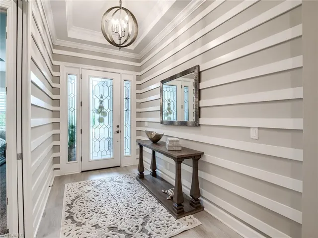 Foyer with a tray ceiling, plenty of natural light, light wood-type flooring, and a chandelier