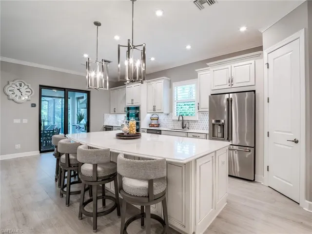 Kitchen featuring tasteful backsplash, stainless steel appliances, decorative light fixtures, a kitchen island, and white cabinetry