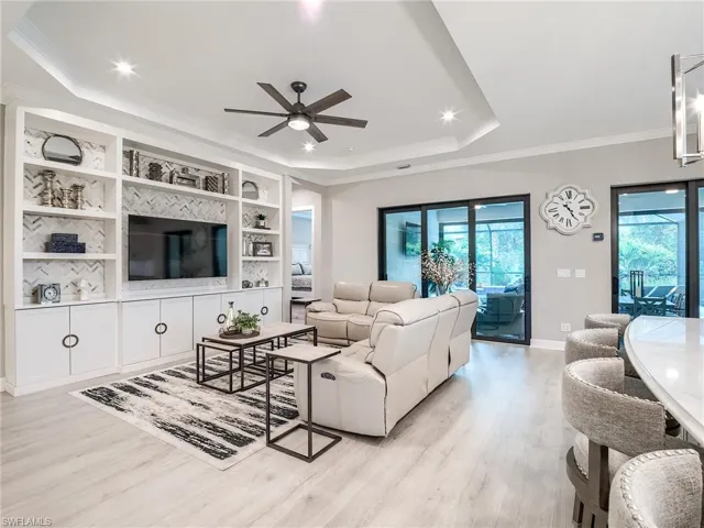 Living room featuring a tray ceiling, light hardwood / wood-style floors, ornamental molding, and ceiling fan
