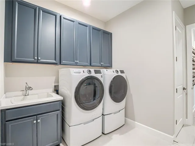 Laundry room featuring separate washer and dryer, cabinets, light tile patterned floors, and sink