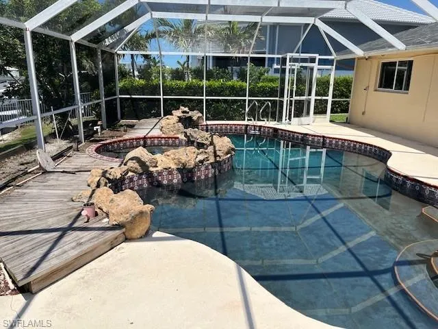 Outdoor pool featuring an in-ground hot tub, a sunroom, glass enclosure, and a patio