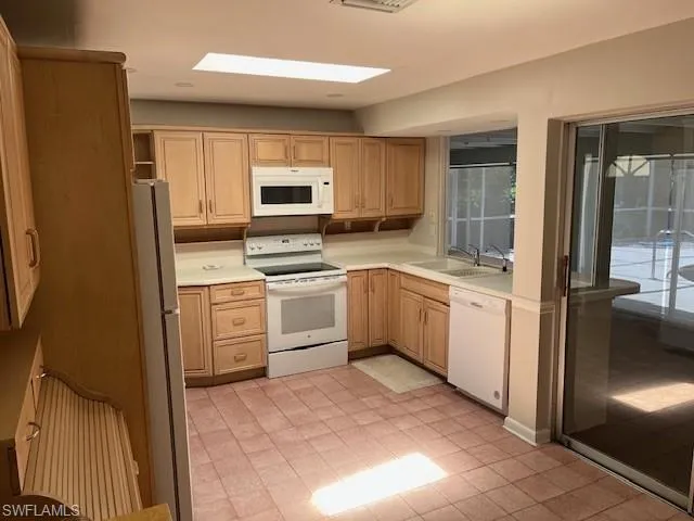 Kitchen with white appliances, light countertops, light brown cabinets, and light tile patterned floors