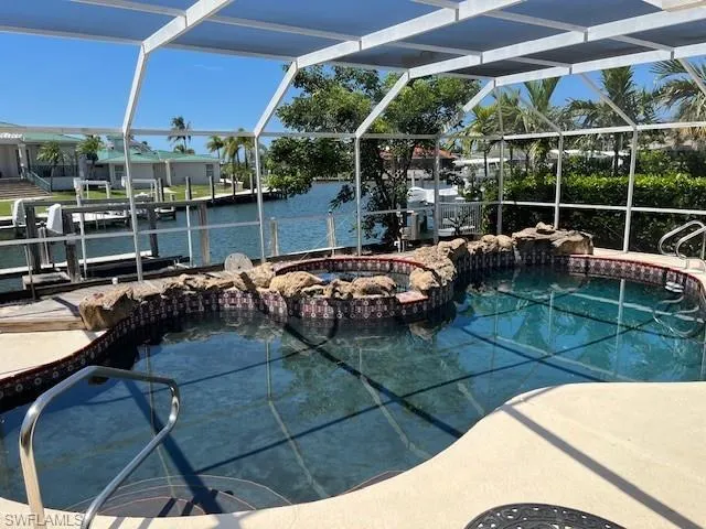 View of swimming pool featuring glass enclosure, a pool with connected hot tub, a sunroom, and a water view