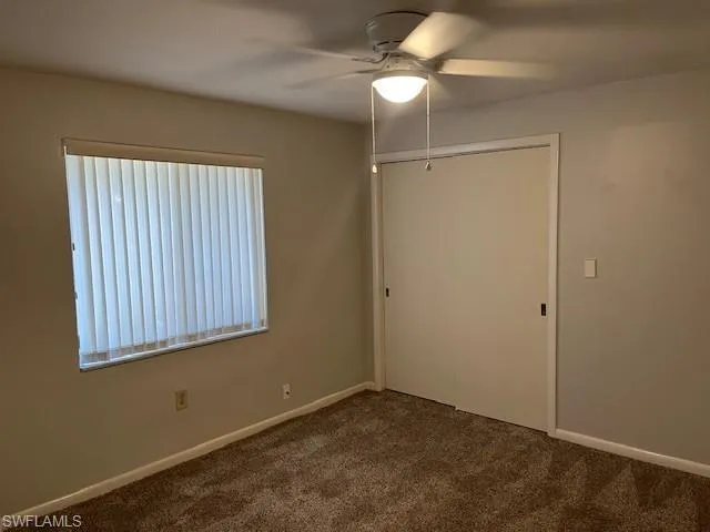 Unfurnished bedroom with dark colored carpet, a closet, and ceiling fan