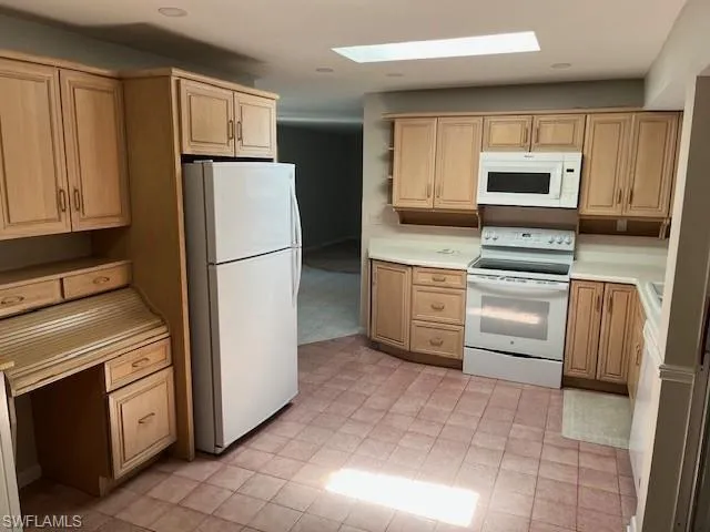 Kitchen featuring white appliances, light countertops, a skylight, built in desk, and light brown cabinetry