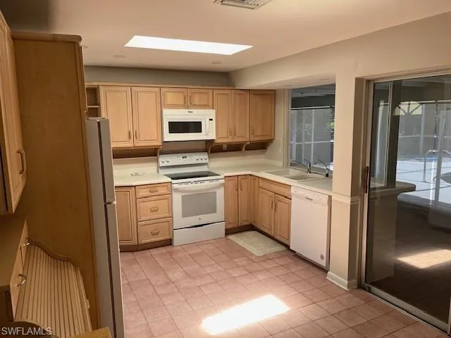 Kitchen featuring white appliances, light countertops, light brown cabinetry, and light tile patterned floors