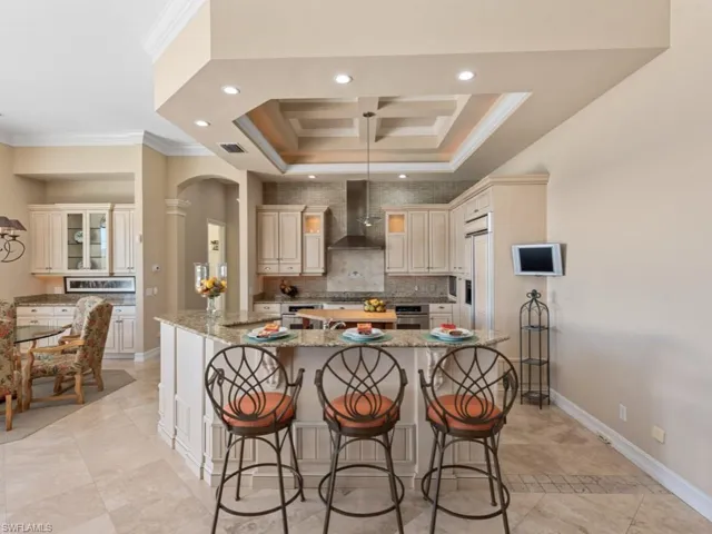 Kitchen with a spacious island, visible vents, crown molding, wall chimney range hood, and a kitchen bar