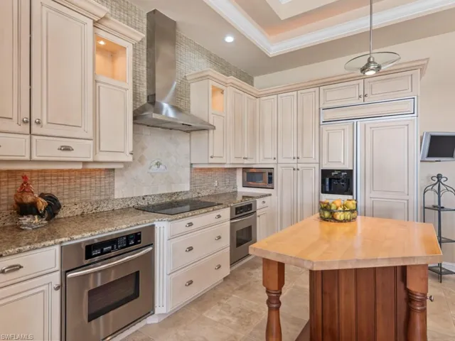 Kitchen featuring wood counters, cream cabinets, stainless steel appliances, wall chimney exhaust hood, and decorative backsplash