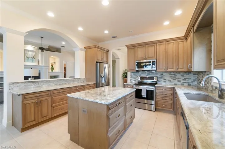 Kitchen with ceiling fan, light stone counters, stainless steel appliances, a kitchen island, and a sink