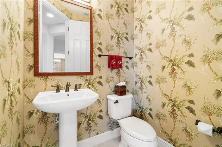 Bathroom with toilet, a sink, visible vents, baseboards, and wallpapered walls