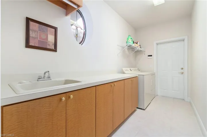 Laundry area featuring cabinet space, light tile patterned floors, baseboards, washer and clothes dryer, and a sink