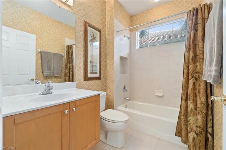 Bathroom with wallpapered walls, toilet, tile patterned floors, shower / bath combo with shower curtain, and vanity