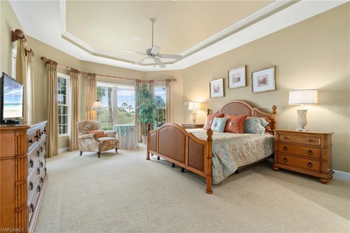 Carpeted bedroom with a tray ceiling, ceiling fan, and baseboards