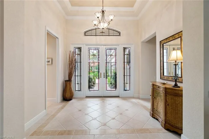 Foyer entrance with a chandelier, light tile patterned flooring, crown molding, and baseboards