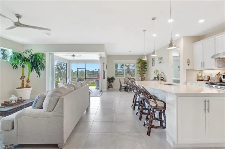 Kitchen with pendant lighting, backsplash, sink, white cabinetry, and a kitchen island with sink