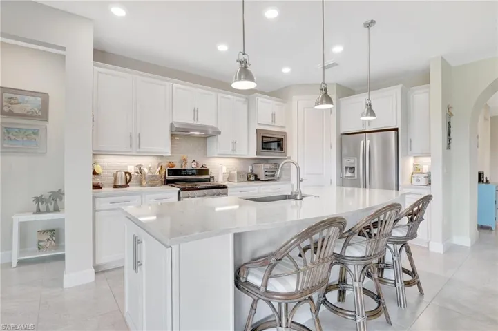 Kitchen with appliances with stainless steel finishes, sink, white cabinetry, hanging light fixtures, and an island with sink