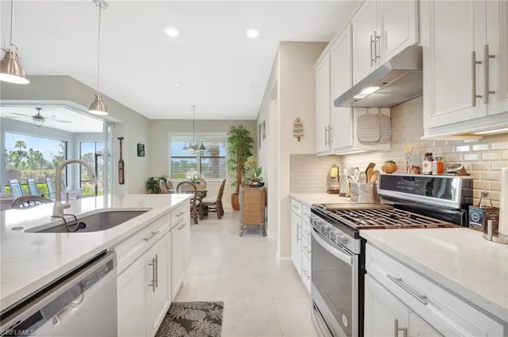 Kitchen with appliances with stainless steel finishes, sink, white cabinetry, hanging light fixtures, and light stone countertops