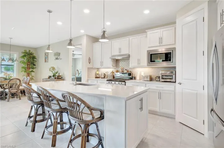 Kitchen featuring a center island with sink, hanging light fixtures, stainless steel appliances, sink, and white cabinetry