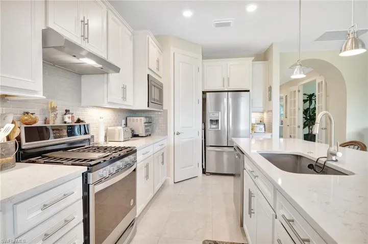 Kitchen featuring appliances with stainless steel finishes, light stone countertops, pendant lighting, sink, and white cabinetry