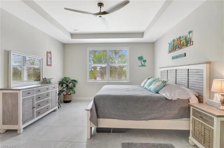 Tiled bedroom with multiple windows, a tray ceiling, and ceiling fan