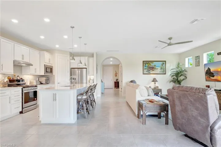 Kitchen featuring an island with sink, white cabinets, stainless steel appliances, and decorative light fixtures