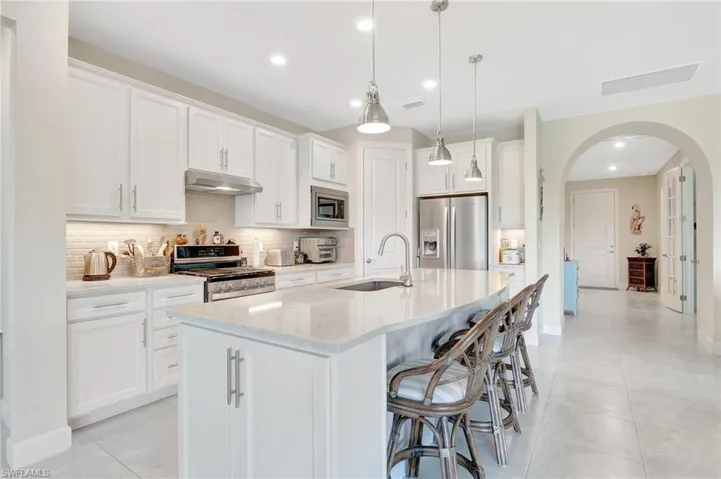 Kitchen featuring white cabinets, stainless steel appliances, a kitchen island with sink, and sink