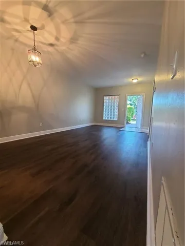 Unfurnished living room featuring dark wood-type flooring and a chandelier