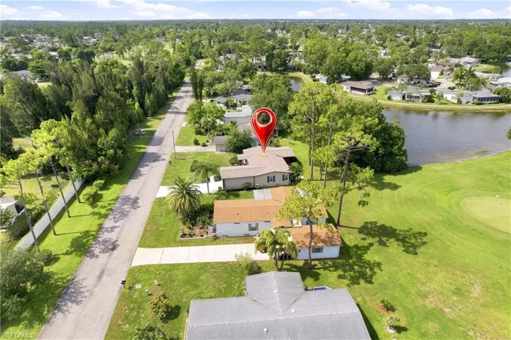 Aerial view of the neighborhood featuring a golf course, a body of water, and mature trees