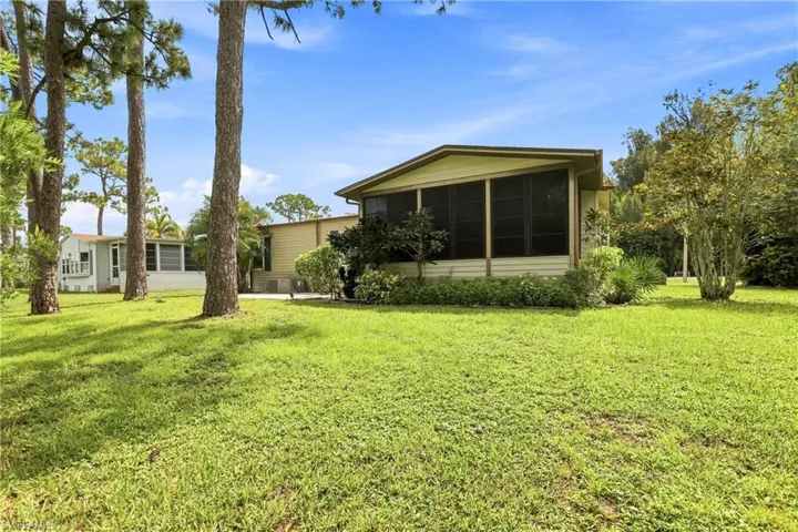 Spacious exterior featuring a screened porch, verdant lawn, mature trees, and established landscaping