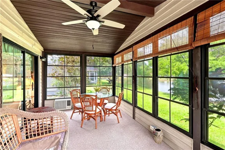 Enclosed patio featuring extensive window panels, vaulted wood-finish ceiling, and ceiling fan with integrated lighting