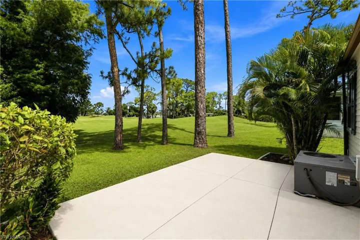 Spacious concrete patio with a manicured lawn, established pine trees, palm foliage, and dense shrubbery