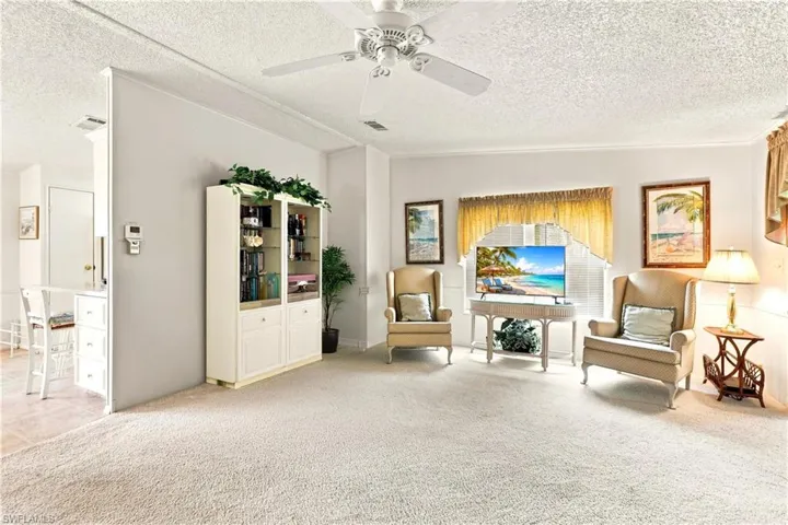 Carpeted living area featuring white walls, a built-in display cabinet, and a ceiling fan