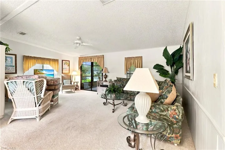 Spacious living area featuring light-toned carpeting, white walls, and a vaulted ceiling with a ceiling fan