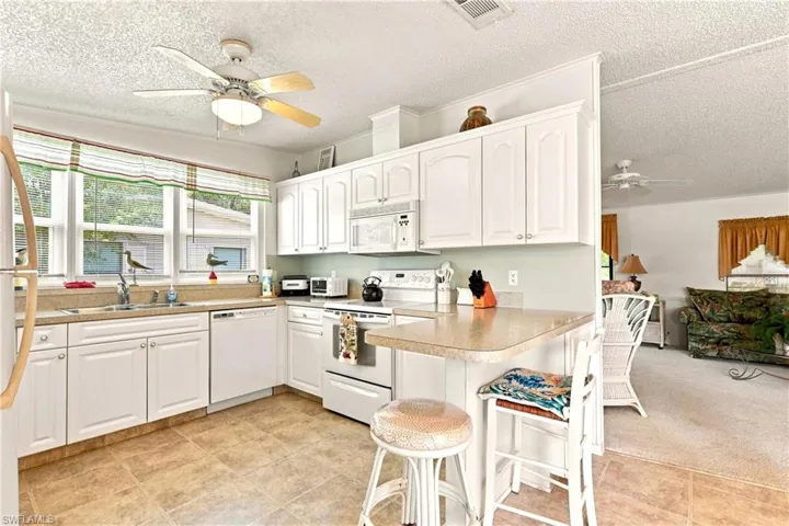 Bright kitchen featuring white cabinetry, a built-in oven, countertop bar seating, and tile flooring