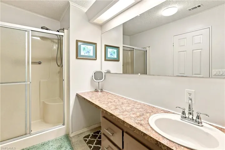 Bathroom featuring a shower enclosure with sliding frosted glass doors, an elongated vanity with a built-in sink, a large wall-mounted mirror, and overhead strip lighting