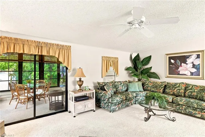 Living space featuring a white ceiling fan, white wall paint, and white textured carpeting